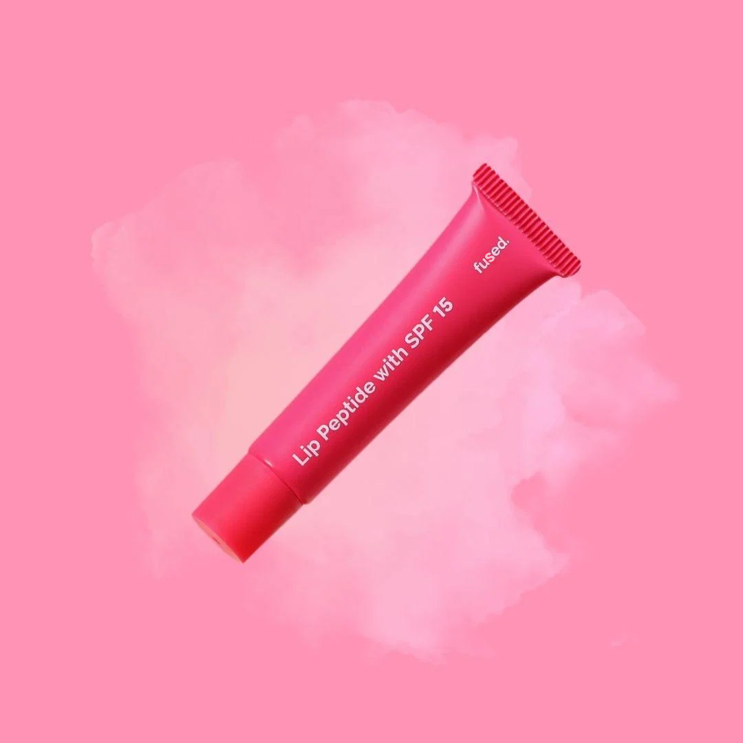 Fused Lip Peptide with SPF 15 pink squeeze tube displayed on a soft pink watercolor aesthetic background